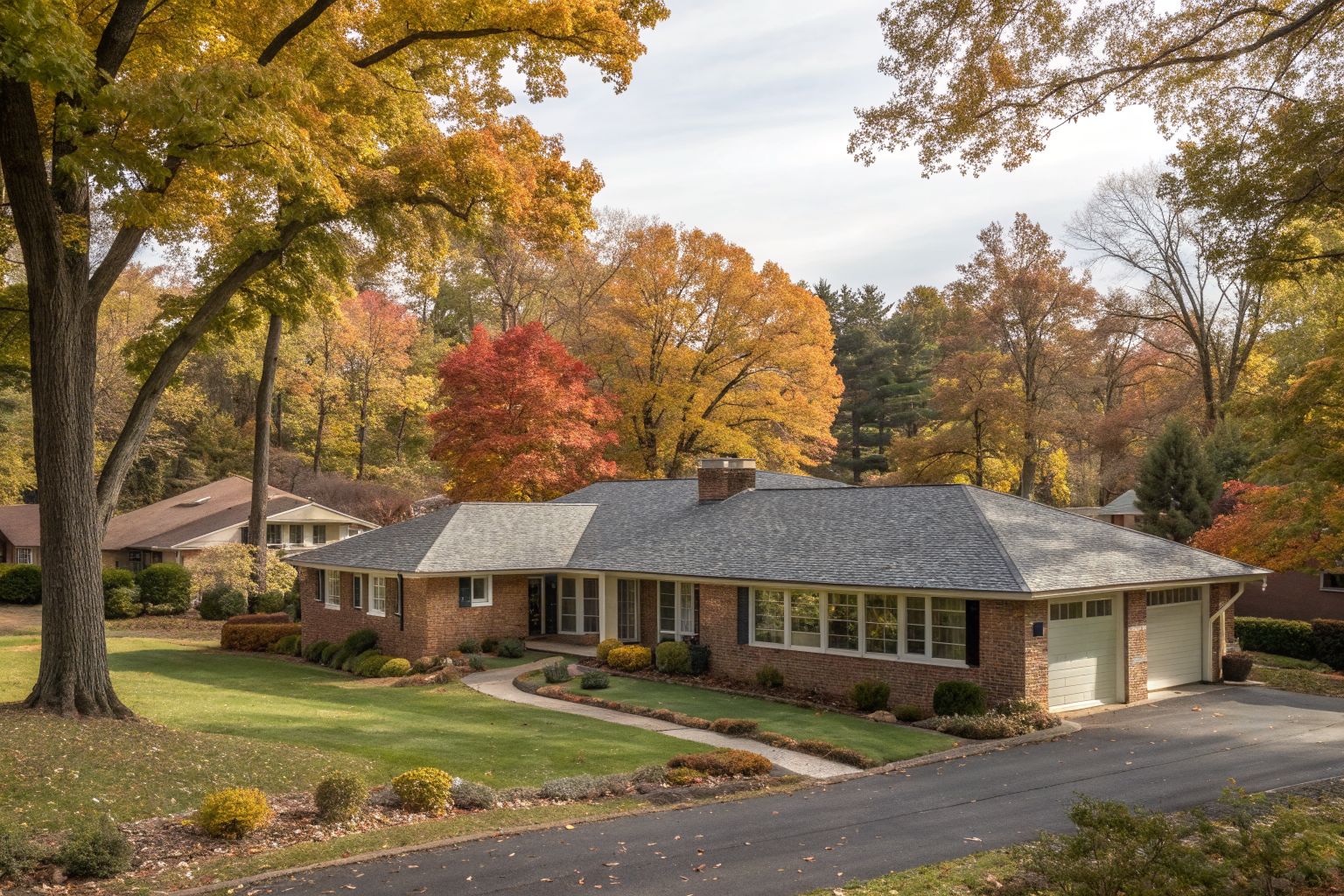 A 1950s brick ranch house with a long low gray shingle roof in autumn